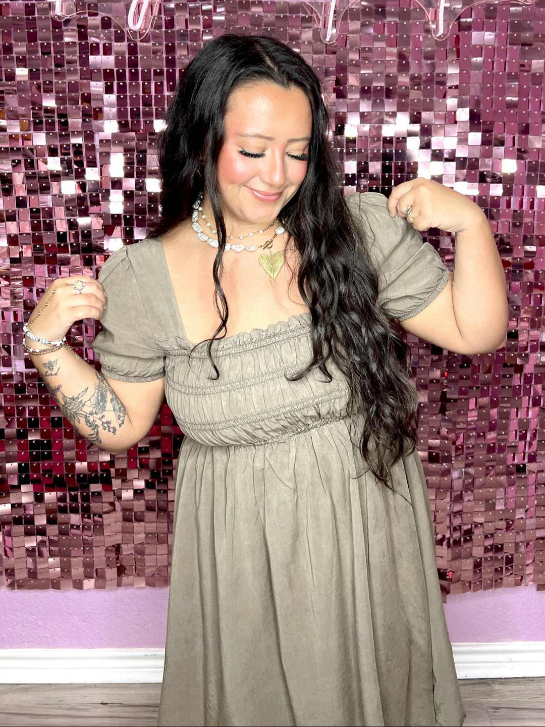 Woman in a gray dress posing in front of a pink mosaic wall with 'Pug on a Pontoon' text.