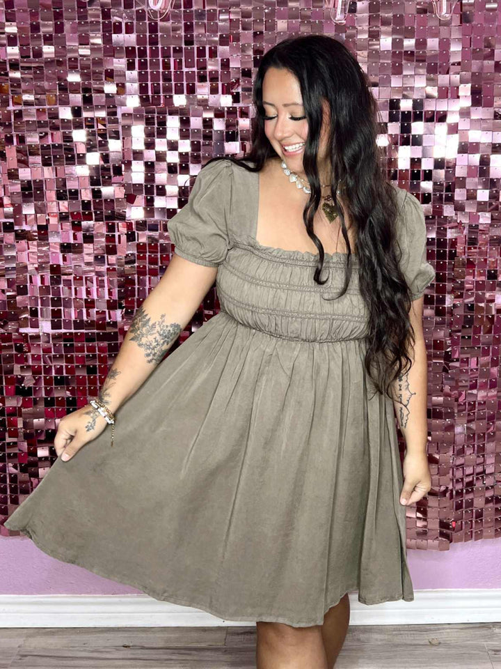 Woman in a green dress standing in front of a pink mosaic wall with 'Pug on a Penthouse' text.