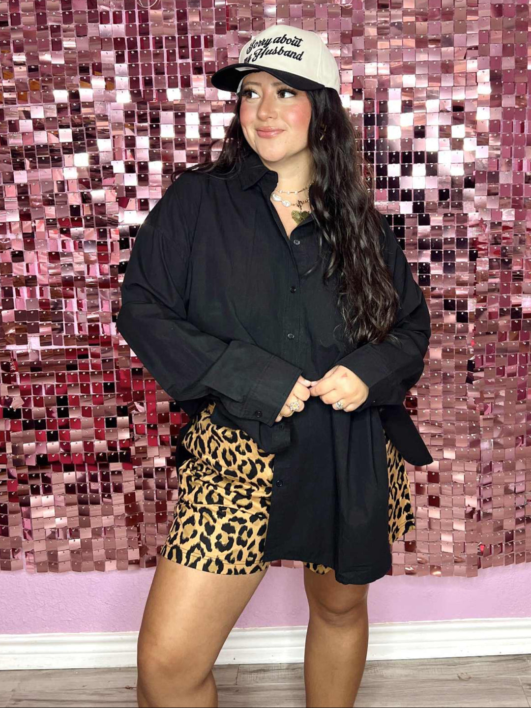 Person wearing a black jacket, leopard print shorts, and a cap in front of a pink mosaic wall with 'Pug on a Pontoon' text.