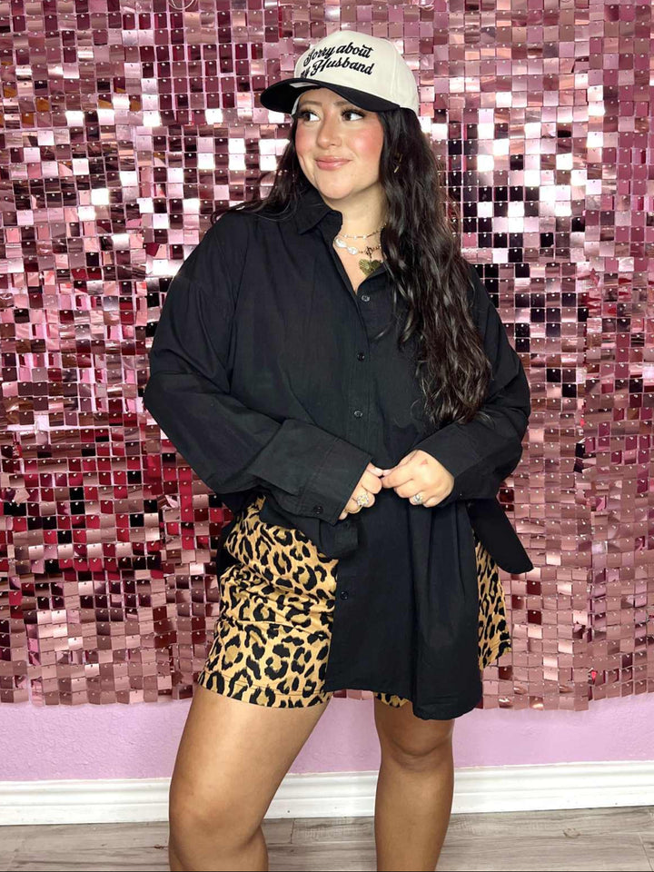 Person wearing a black jacket, leopard print shorts, and a cap in front of a pink mosaic wall with 'Pug on a Pontoon' text.