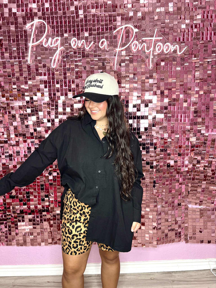 Person wearing a black shirt, leopard print shorts, and a cap in front of a pink mosaic wall with 'Pug on a Pontoon' text.